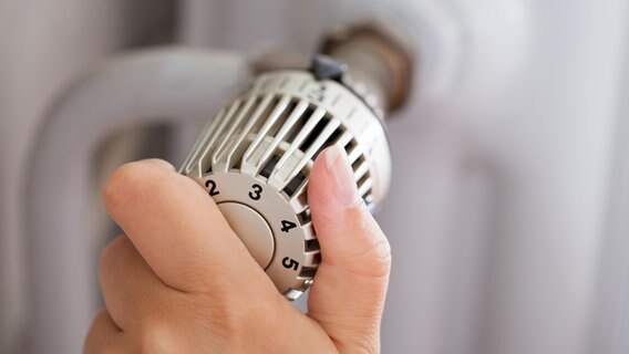 Jemand reguliert mit der Hand eine Heizung am Thermostat. © fotolia.com Foto: Andrey Popov