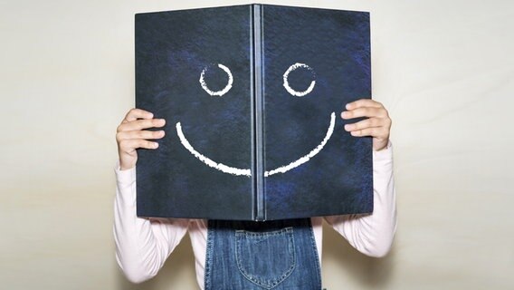 Person hält aufgeschlagenes Buch, auf das ein Smiley gezeichnet ist. © Fotolia.com Foto: JorgeAlejandro
